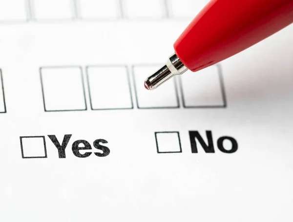 Hand holding red ballpoint pen over Yes and No checkboxes in a form making a decision