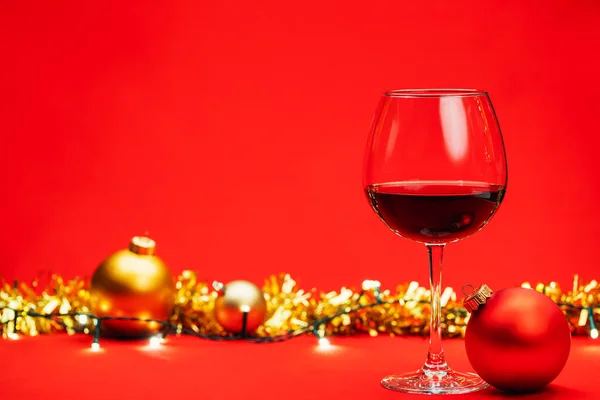 Glas Rode Wijn Met Kerstballen Tinsel Verlichting Rode Achtergrond Kerstdrank — Stockfoto