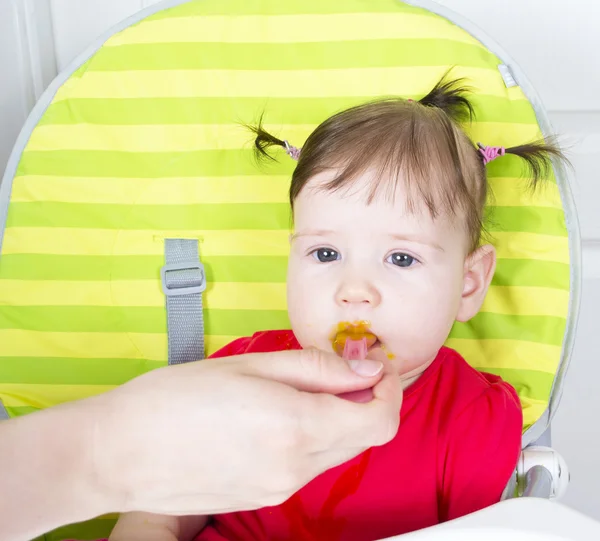 Menina bebê comendo um purê de legumes em uma cadeira alta — Fotografia de Stock