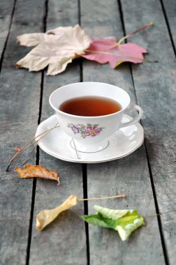 Beyaz bir vintage fincan çay gri rustik ahşap tablo ile sonbahar yaprakları.