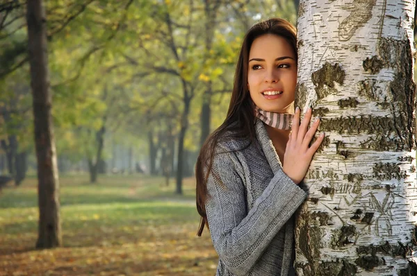 Beautiful woman smiling, leaned on a birch tree — Stock Photo, Image