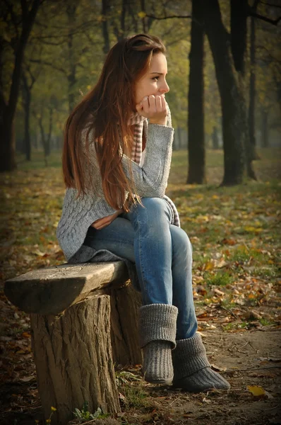 Mujer pensativa sentada en el banco en el parque de otoño — Foto de Stock