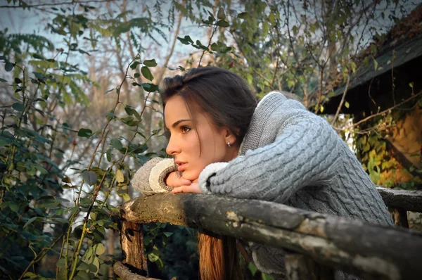 Beautiful woman leaning chin on old wooden fence, thinking — Stock Photo, Image