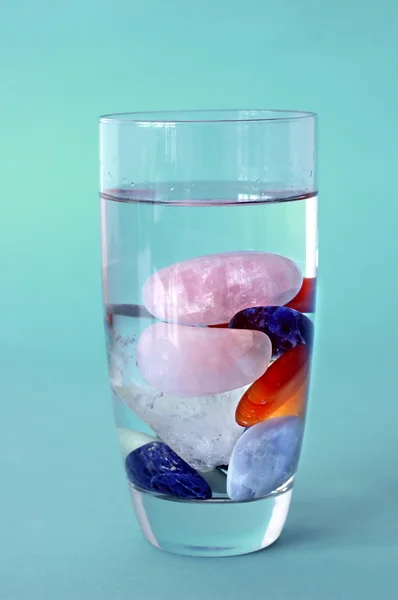 Crystals in full filled glass of water, with green-blue background — Stock Photo, Image