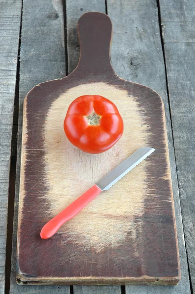 Помидор с красным ножом на старой доске — стоковое фото