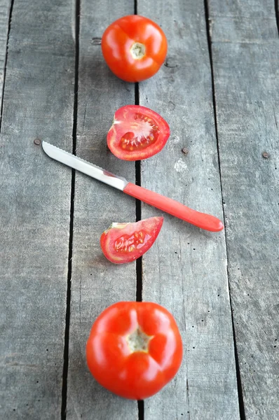 Целые и нарезанные помидоры на сером деревянном фоне — стоковое фото