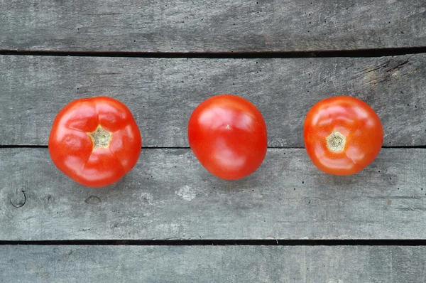Три помидора на сером деревянном фоне — стоковое фото