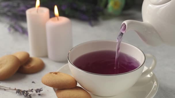 na bílém stole mezi květy levandulového hrnku s levandulovým čajem. Poblíž jsou zapálené svíčky a sušenky