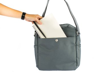 Kadın elinin izole edilmiş yakın çekim görüntüleri defter ve kalemi beyaz arka planda uzun omuz askısı olan küçük şehir iş kadını gri çantasının ön cebine koyuyor..