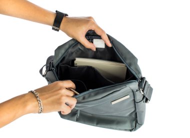 Kadın ellerinin izole edilmiş yakın çekim görüntüleri dokunmatik ekran tableti ve defteri beyaz arka planda boş logo etiketi olan günlük gri iş çantasının içine koyuyor..