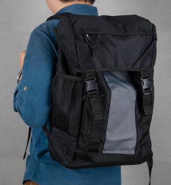 Model standın yakın çekimleri moda şehir modasına uygun siyah ve gri renkli unisex seyahat sırt çantalarını gri arka planda asıyor..