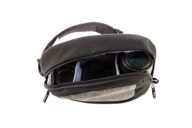 Profesyonel fotoğrafçının, su geçirmez, modaya uygun siyah kumaşlı orta boy sırt çantasının, beyaz arka plandaki yumuşak bölmenin içinde kamera ve lens tutarken çekilmiş yakın çekim görüntüleri..