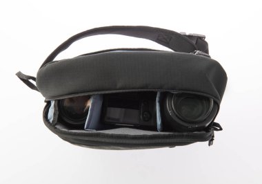 Profesyonel fotoğrafçının, su geçirmez, modaya uygun siyah kumaşlı orta boy sırt çantasının, beyaz arka plandaki yumuşak bölmenin içinde kamera ve lens tutarken çekilmiş yakın çekim görüntüleri..