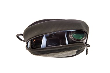 Profesyonel fotoğrafçının, su geçirmez, modaya uygun siyah kumaşlı orta boy sırt çantasının, beyaz arka plandaki yumuşak bölmenin içinde kamera ve lens tutarken çekilmiş yakın çekim görüntüleri..