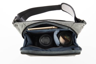 Küçük fotoğrafçı yakın çekim stüdyosu modern moda gri şok geçirmez bel çantası yumuşak bel çantası dijital DSR kamera len ve akıllı telefonu beyaz arka planda taşıyor..