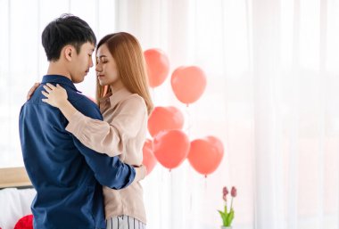 Sevgililer Günü 'nde romantik bir randevu sırasında ışık odasında gözleri kapalı dans eden Asyalı erkek ve kadının yan görüntüsü