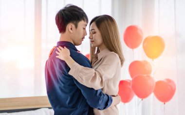 Sevgililer Günü 'nde romantik bir randevu sırasında ışık odasında gözleri kapalı dans eden Asyalı erkek ve kadının yan görüntüsü