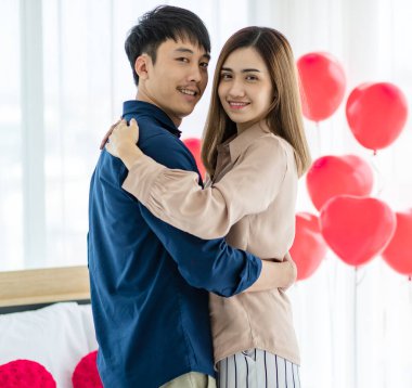 Sevgililer Günü 'nde romantik bir randevu sırasında Asyalı kadın ve erkeğin dans edişinin ve ışık odasında kameraya bakışımızın yan görüntüsü.