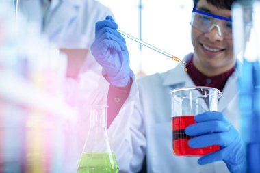 Laboratuvarda iş arkadaşlarıyla kimyasalları karıştıran Asyalı erkek bilim adamının yumuşak odak noktası.