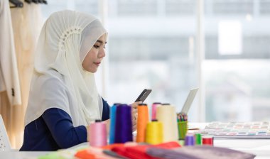 Mutlu Müslüman kadın tasarımcı atölyede masa başında çalışırken işine konsantre oluyor.