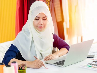 Mutlu Müslüman kadın tasarımcı atölyede çalışırken iş çizimi ve çizim modeline konsantre oluyor.