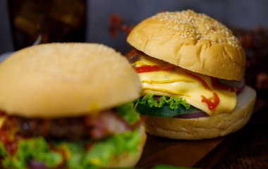 Ev yapımı hamburger ve arka planda bir bardak içecekle taze malzemeler yemeye hazır. Koyu renkli ışık ile çekilmiş.