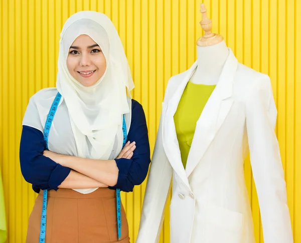 自信に満ちたイスラム教徒の女性でヒジャーブ交差腕と笑顔でカメラを見ながら近くに立ってマネキンと黄色の壁に対するカスタムスーツでアトリエ — ストック写真