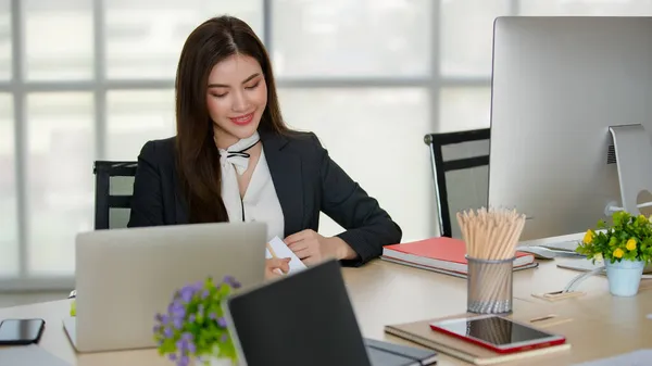 ブラックビジネスの若い魅力的なアジアの女性は コンピュータやラップトップがぼやけた窓の背景を持つモダンな外観のオフィスで働いているテーブルの後ろに座っています 現代オフィスライフスタイルのコンセプト — ストック写真