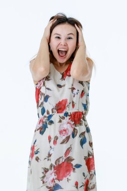 Beyaz çiçek desenli elbise giymiş Asyalı çılgın çılgın kadın modelin el ele tutuşup çığlık atarak beyaz arka plandaki kameraya bağırdığı tek bir portre çekimi..
