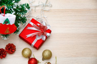 Noel dekoratif eşyaları, kırmızı ve altın renkli parlak küreler, mumlar, hediye paketi, gümüş kurdele, papyon, ip, çam tohumları, ahşap masa üzerinde asılı çorap, Noel ağacı..