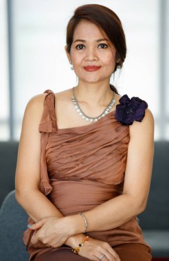 50 'lerin Asyalı klas portresi güzel yönetici kadın kendinden emin ve gururlu bir şekilde gülümsüyor, iç odadaki kanepede oturuyor, iyi giyiniyor ve şık aksesuarları fotokopi alanı ile takıyor.