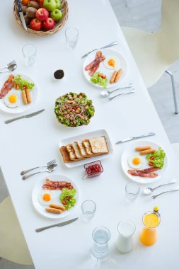 En üstte, ev yapımı beyaz masada servis edilen dört kahvaltılık hava manzarası kızarmış yumurta, domuz pastırması, kaşıklı sosis, çatal ve bıçaklardan oluşuyor. Ekmek, sağlıklı salata, elma ve elmayla süslenmiş.