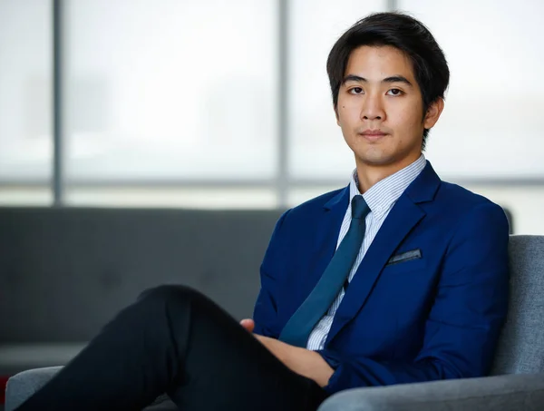 20代の先見の明のある若いハンサムなアジアの経営者は 正式なスーツを着て リラックスして快適な足の上に座って 成功への決意と自信を持ってカメラを見て — ストック写真