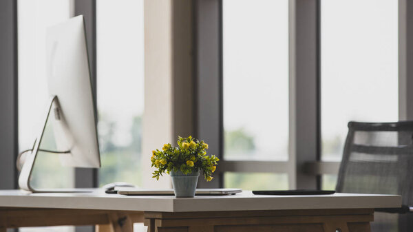 Selective focus beautiful refresh yellow flowers in vase decorated on a modern desk with a computer in a comfortable office at daytime. Presenting creative interior design, good working environment