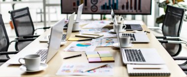 Laptop bilgisayarlar ve beyaz kahve fincanları çalışma masasının üzerine yerleştirilmiş kağıt kağıtlarıyla dolu büyük ekrandaki hedef büyüme oranı grafiği ve grafiğinin önündeki toplantı odasında rapor edilen belgeler..