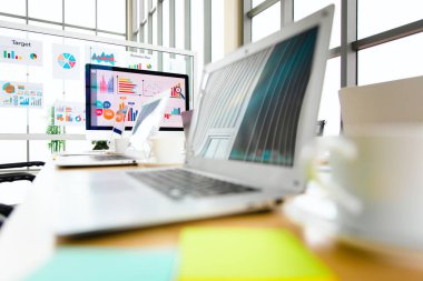 Bilgisayarın renkli dizüstü bilgisayarı, kağıt rapor grafiği dokümanları konferans salonundaki masanın üzerine yerleştirilmiş analiz satış hedefleri ekranda ve cam panoda bulanık arka planda..