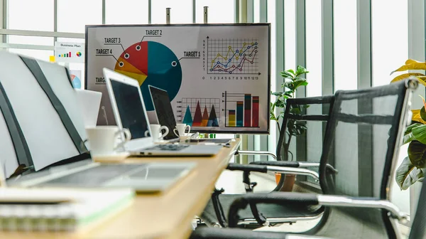 Laptop bilgisayarlar ve beyaz sıcak kahve fincanları çalışma masasının üzerine yerleştirildi konferans odasında ön yatırım hedef büyüme hızı grafiği ve grafiği ekranda ve güvertede yayınlandı..