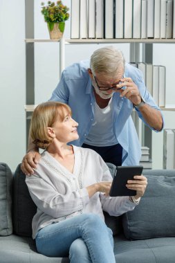 Kafkasyalı yaşlı, yaşlı, yaşlı, mutlu eş koltukta oturuyor tablet bilgisayarda gri sakallılara bilgi gösteriyor ve saç teli takan koca ona bakıyor..