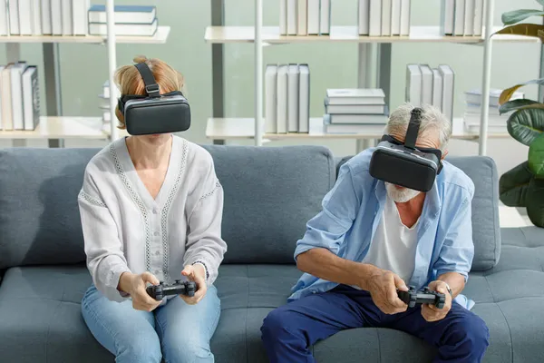 白种人老年祖父母夫妇戴着虚拟现实的护目镜耳机 灰胡子和头发爷爷和奶奶的妻子在客厅里拿着操纵杆玩电子游戏 — 图库照片