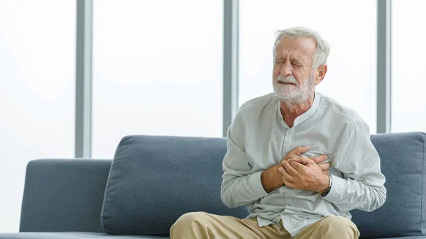 白人高齢者の不健康な病気男性の夫おじいちゃんは自宅でソファに座っているだけで胸に手をつないで緊急心臓発作の病気に苦しんでいる — ストック写真