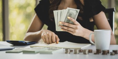 Yakın plan çekimde, regkonansız bir kadın gelir harcamalarını, elinde para notlarını ve ofiste muhasebe kavramını hesaplamak için hesap makinesi kullanıyor..