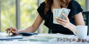 Yakın plan çekimde, regkonansız bir kadın gelir harcamalarını, elinde para notlarını ve ofiste muhasebe kavramını hesaplamak için hesap makinesi kullanıyor..