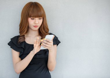 Genç ve sevimli Asyalı, esmer, siyah elbiseli, ayakta duran, kullanan, mesajlaşan ve kayan akıllı telefonlu bir kadın..