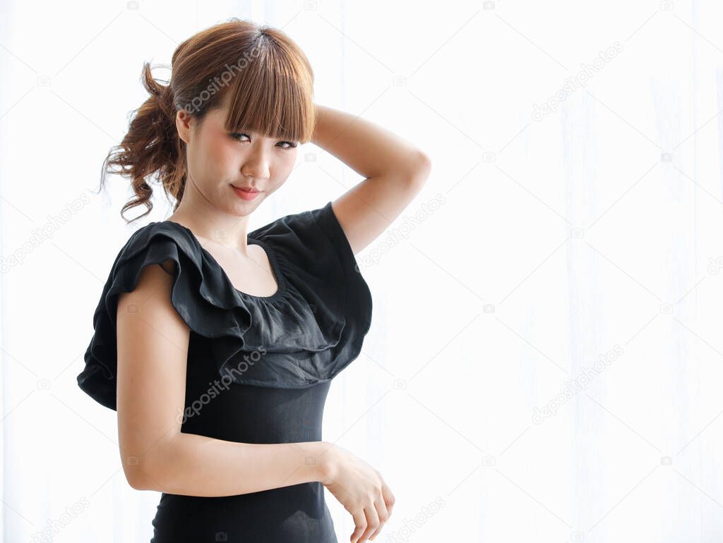 Lovely cute Asian woman in black dress using her hand to gather brunette hair and play on it  with happy and funny for show her beautiful hairstyle.