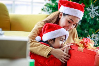 Mutlu Asyalı aile kızı süveter giyip Noel Baba şapkası takıyor. Annesiyle birlikte oturuyor. Hediye kutusunu açtığında heyecanlanıyor..