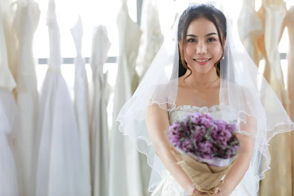 白いドレスでアジアの美しい花嫁の手の中に開催された紫色の結婚式の花の花束のショットを閉じます — ストック写真