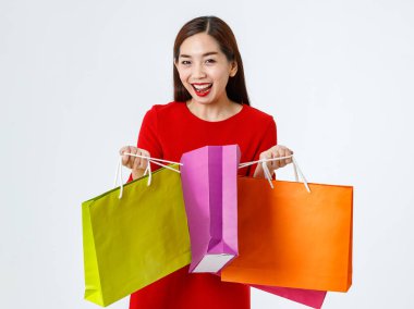 Sevimli ve neşeli Asyalı bayan müşteri ya da alıcı kağıt alışveriş torbalarına bakıyor ve stüdyodaki beyaz arka plandaki alışverişlerden keyif alıyor.