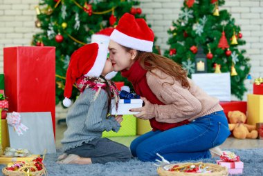 Çekici Asyalı anne ve kız kış kıyafetleri giyip Noel Baba 'nın şapkası ile Noel' i neşe ve mutluluk içinde ve süslü Noel ağacı arka planıyla kutluyorlar. Aile Noel partisi kavramı.