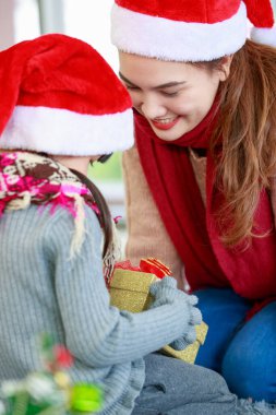 Çekici Asyalı anne-kız kışlık kıyafetler giyiyorlar ve Noel Baba 'nın şapkasıyla Noel' i neşeyle kutluyorlar. Süslü Noel ağacı arka planı. Aile Noel partisi kavramı.