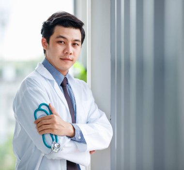 Medikal odasında steteskopla dikilip bakışlarını kaçıran düşünceli Asyalı erkek sıhhiyeci.